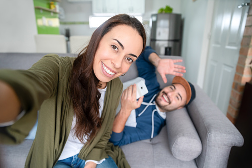 Happy Latin American couple at home on a video call and waving to the camera while smiling - lifestyle concepts