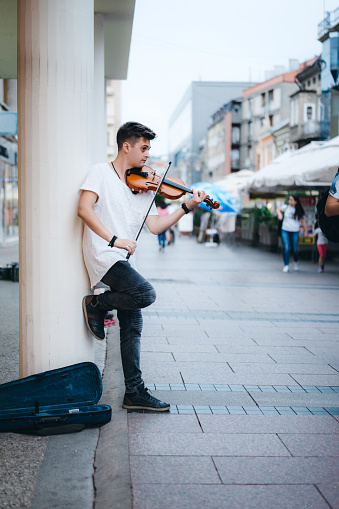 Young Caucasian man playing violin on a city street for money.