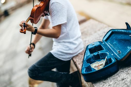 Young Caucasian man playing violin outdoor for money.