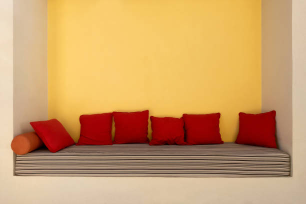 Empty comfortable niche couch with striped cushioned mattress and red soft pillows. Modern sofa with nobody sits on it in summer resort town outdoors.