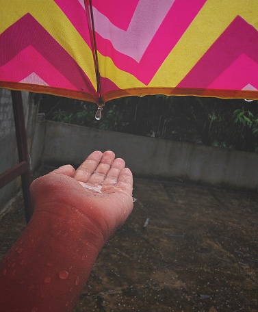 Woman standing with umbrella and enjoying rainy season at home terrece