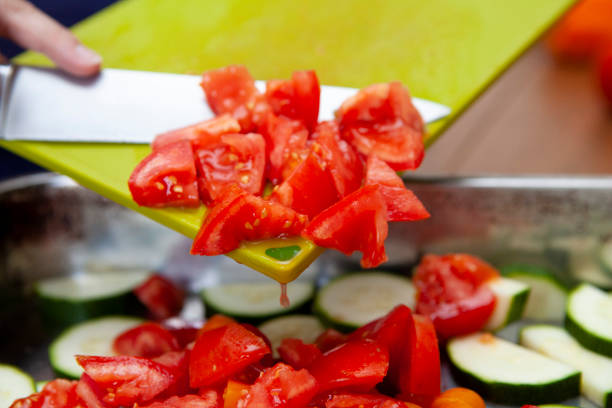 Roughly chopped tomato falling off a cutting board into a stainless steel pan