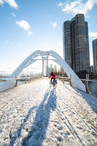 Toronto, Ontario - December 5, 2019 : A cyclist crossing the Humber Bay Arch Bridge south of Lake Shore Boulevard West, in west Toronto. Icy and snowy conditions.