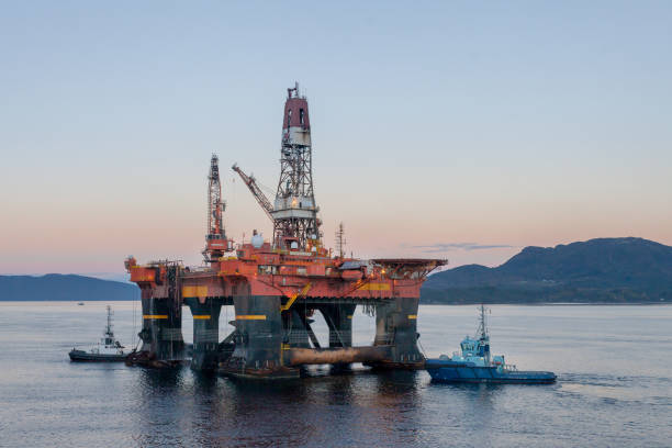 The semi-submersible drilling rig West Alpha inside the Norwegian fjord in the morning with tug boats. OELEN NORWAY - 2014 OCTOBER 16. The semi-submersible drilling rig West Alpha inside the Norwegian fjord in the morning with tug boats. oil derrick crane crane exploration stock pictures, royalty-free photos & images