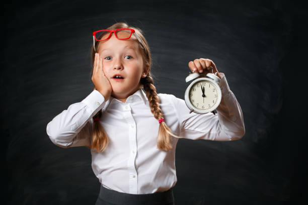 Back to school. Funny little girl schoolgirl with an alarm clock on the background of a black chalk board. The shocked child worries about the deadline Back to school. Funny little girl schoolgirl with an alarm clock on the background of a black chalk board. The shocked child worries about the deadline. blackboard child shock screaming stock pictures, royalty-free photos & images