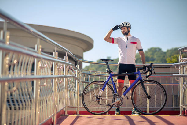 Attractive cyclist with bike exploring the area Nice place. Attractive athletic cyclist with bike standing with hand near eyes looking over terrain top view on people walking and cyclists riding stock pictures, royalty-free photos & images
