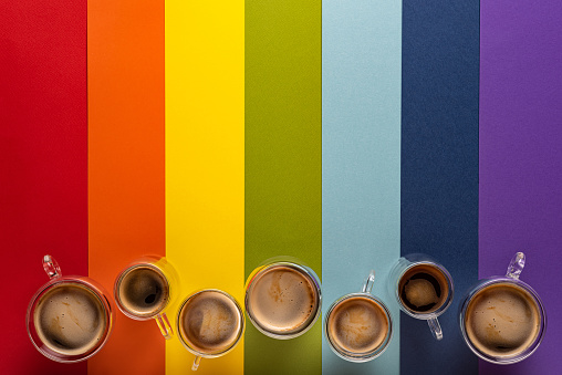 Row of thermo glass cups with fresh black espresso and americano coffee. Colorful striped background in LGBT colors with paper texture. Directly above view. Large copy space. LGBT community concept.