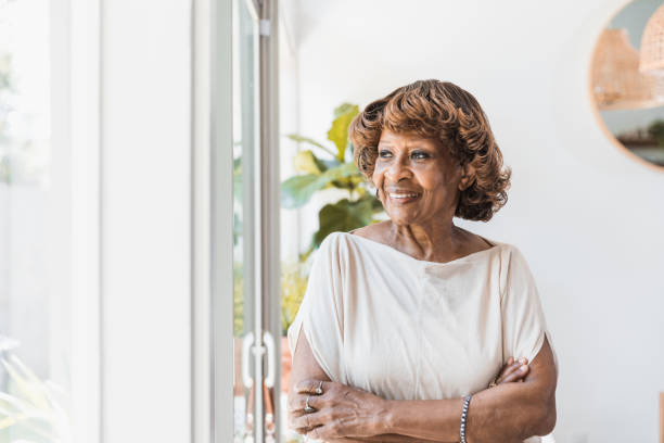 istock Confident senior woman stands by windows at home 1266123447