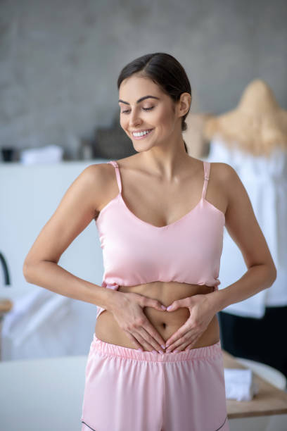 istock Woman in pink touching her abdomen and smiling 1266123777