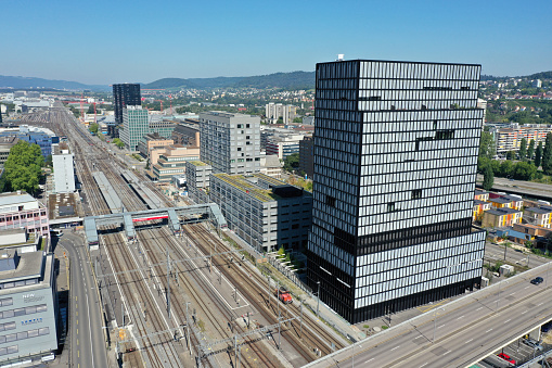 Zürich Altstetten with an office building in the foreground and the railway station in the background. The wide angle image was captured during summer season.