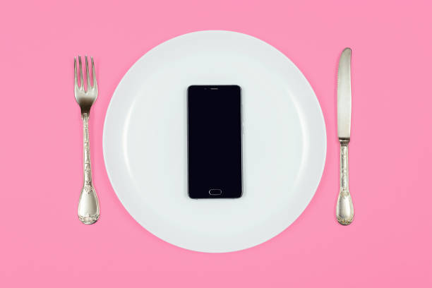istock Black smartphone on white plate with fork and knife 1266137771