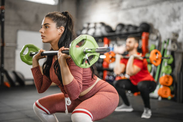 ジムでのクロストレーニングでバーベルで強さを行使する2人の若いアスリート - weight training crouching barbell weightlifting ストックフォトと画像