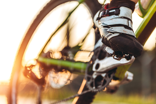 Caucasian cyclist riding a bike on road at sunset. Close up of foots on bicycle pedals.