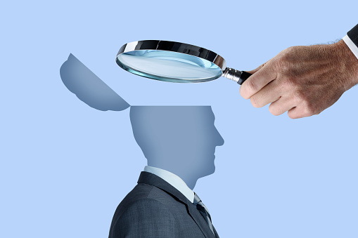 A man uses a magnifying glass to peer into the open mind of a human being.