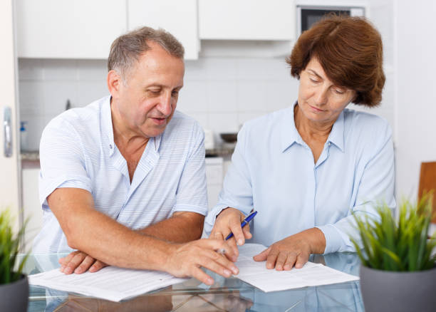 istock Mature family couple sitting at kitchen table and  signing documents 1266146671
