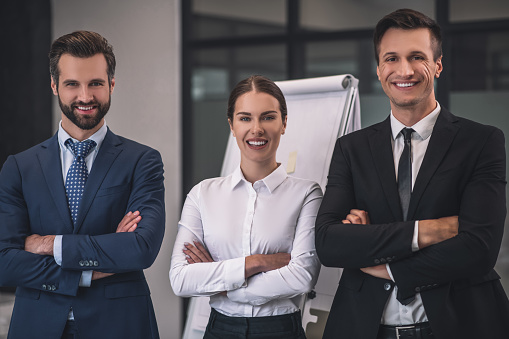 Best team. Brown-haired female and two male colleagues standing with folded arms, smiling