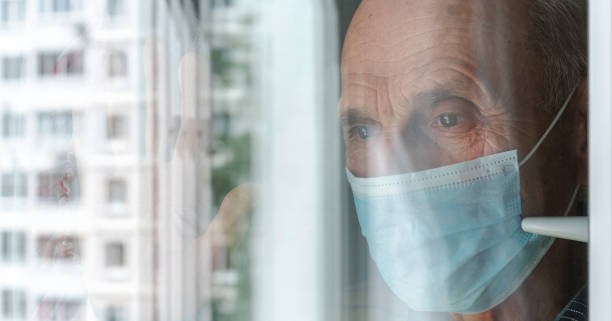 istock old man with sad eyes in mask stands behind window glass 1266158635
