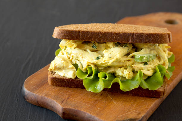 istock Homemade Coronation Chicken Sandwich on a rustic wooden board on a black background, low angle view. Close-up. 1266159485