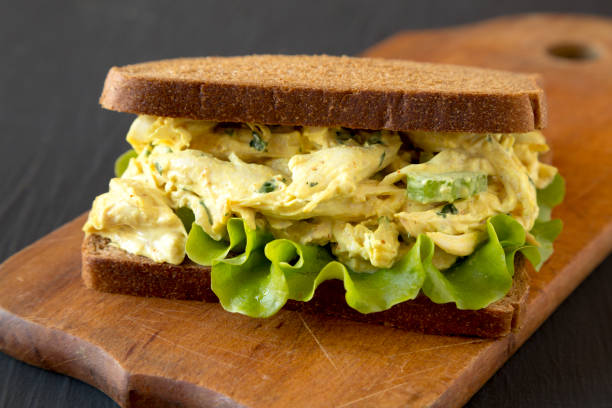 istock Homemade Coronation Chicken Sandwich on a rustic wooden board on a black surface, low angle view. Close-up. 1266159583