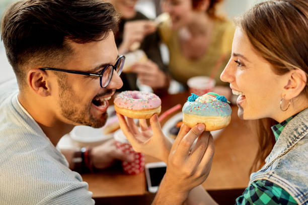 istock Carefree couple feeding each other with a donuts in a cafe. 1266159984