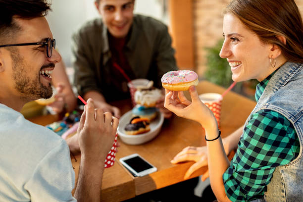 istock Happy couple talking while eating donuts with friends in a cafe, 1266161327