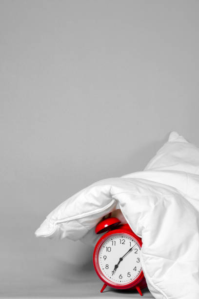 Alarm clock under the pillow - Don't want to wake up concept Close-up of a red alarm clock under the pillow. Don't want to wake up concept. Space for copy. cross off stock pictures, royalty-free photos & images