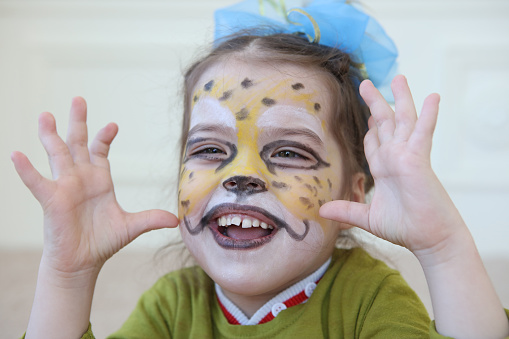 Close-up of smiling little girl with her face painted like a cheetah. Shallow depth of field.