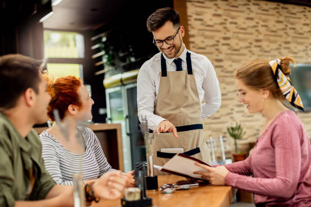 istock Young happy waiter communicating with group of customers in a cafe. 1266161769