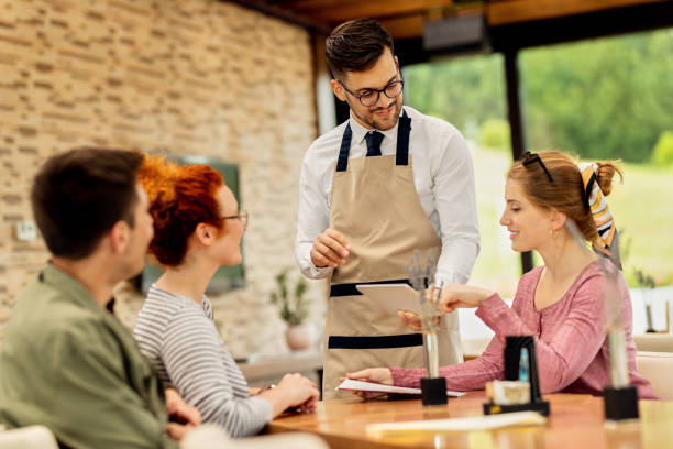 istock Young waiter showing menu on touchpad to his customers in a cafe. 1266161910