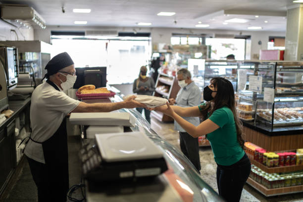 istock Baker passing a bag of bread to a customer using face mask 1266164165