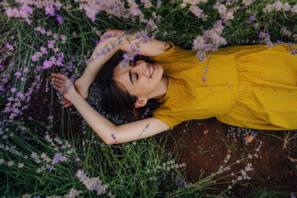 Into the loving arms of nature Photo of a smiling young woman lying in lavender; enjoying the beautiful and peaceful weekend getaway, far from the hustle of the city. women healthy lifestyle beauty nature stock pictures, royalty-free photos & images