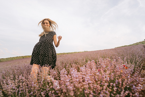 Photo of a smiling young woman running through the lavender field; enjoying the beautiful and peaceful weekend getaway, far from the hustle of the city.