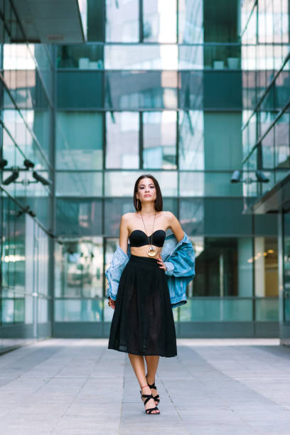 A young woman in bright clothes, a red skirt and a green longsleeve is standing in a business center. High-heeled shoes