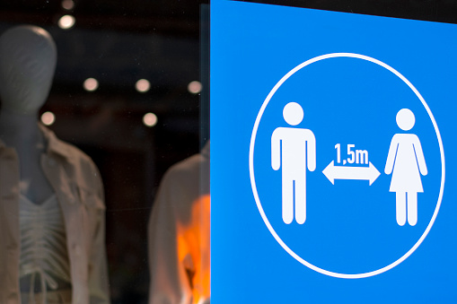 A social distancing poster with illustration on a window of a clothing store to guide social distancing 1.5 meters due to coronavirus or covid-19 pandemic and indicating how much distance people should keep to be safe.