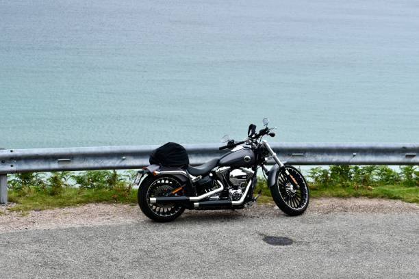 Scotland / United Kingdom - August 04, 2020: Grey Motorbike parked by the road barrier next to cliff overlooking to turquoise sea