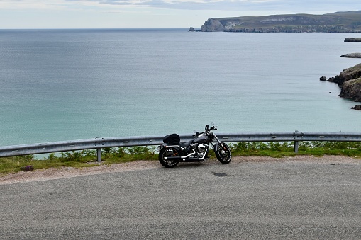 Scotland / United Kingdom - August 04, 2020: Panoramic view of Scotland turquoise color sea and cliffs from high ground wıth a grey motorbike by the road