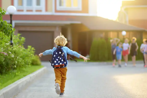 Photo of Little schoolboy joyfully running to school after holiday. Child meeting with friends. Education for children. Back to school concept.