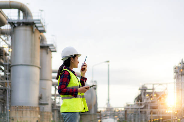 istock Asian woman technician Industrial engineer using walkie-talkie and holding bluprint working in oil refinery for building site survey in civil engineering project. 1266182465