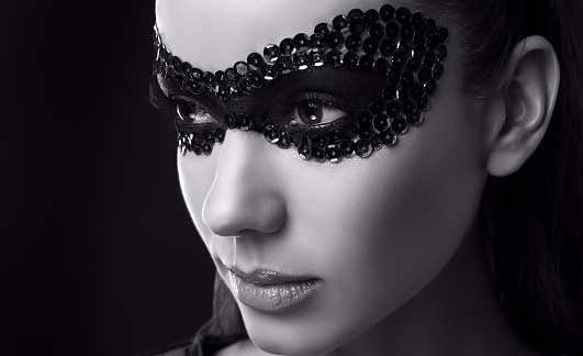 Close-up portrait of charming elegant brunette woman in sequins mask posing on black background in studio
