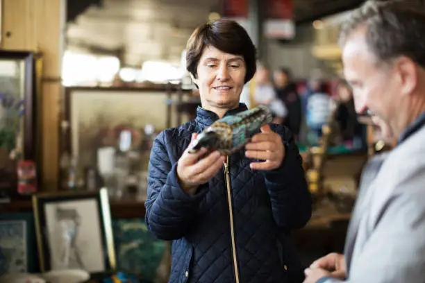 Mature woman is visiting the market of old things and choosing casket outdoors