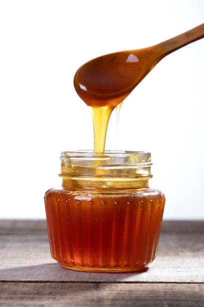 istock Honey dripping from the honey dipper into a glass jar. 1266189142