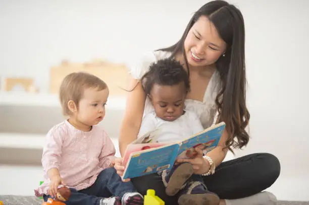 A woman reads a picture book to the babies on her lap.