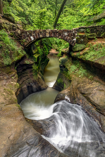 A beautiful rock foot bridge crosses a forest stream at the Devil’s Bathtub, a carved sandstone water feature in the Old Man’s Cave section of Hocking Hills State Park, Ohio.
