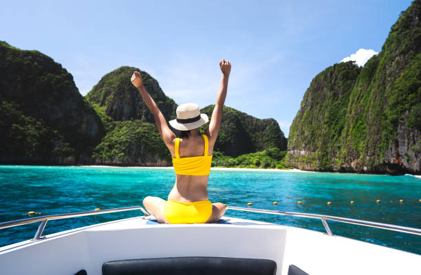 Rear view of adult traveling woman sit and relax arm stretch on the sailing boat at island Rear view of adult traveling woman sit and relax arm stretch on the sailing boat wear yellow bikini blue sky and sea. Summer vacation island domestic trip at Maya bay. Krabi, Thailand phi phi islands stock pictures, royalty-free photos & images