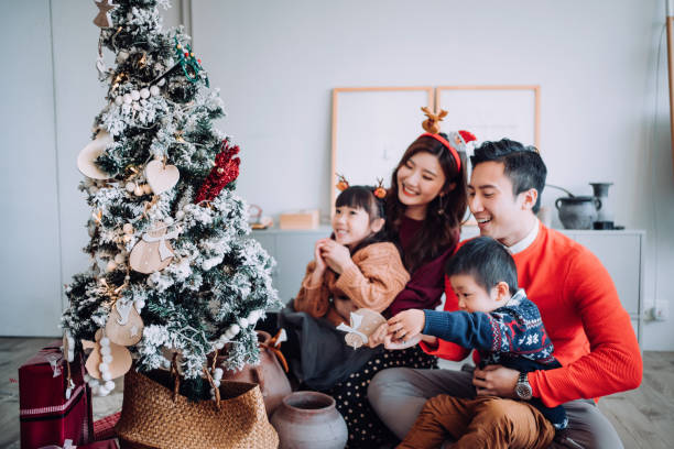 クリスマスライフスタイルのテーマ。自宅のリビングルームで一緒にクリスマスツリーを飾る幸せなアジアの家族。彼らは様々なボーブルや装飾品を着て、彼らの休日を楽しんでいます - christmas theme ストックフォトと画像