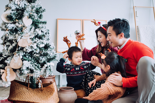 Tema de estilo de vida navideño. Feliz familia asiática decorando árbol de Navidad juntos en la sala de estar en casa. Están poniendo en varias bolas y adornos y disfrutando de sus vacaciones photo