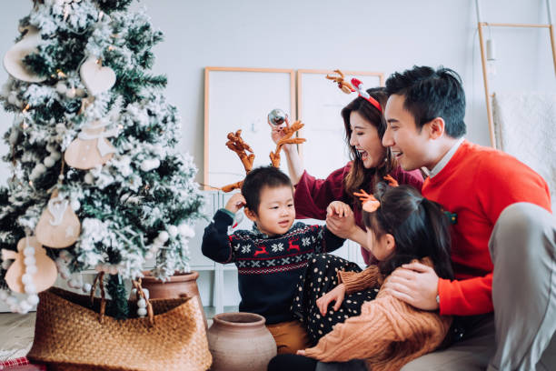 クリスマスライフスタイルのテーマ。自宅のリビングルームで一緒にクリスマスツリーを飾る幸せなアジアの家族。彼らは様々なボーブルや装飾品を着て、彼らの休日を楽しんでいます - 伝統 写真 ストックフォトと画像