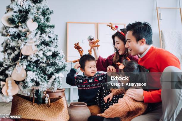 Christmas Lifestyle Theme Happy Asian Family Decorating Christmas Tree Together In The Living Room At Home They Are Putting On Various Baubles And Ornaments And Enjoying Their Holiday Stock Photo - Download Image Now