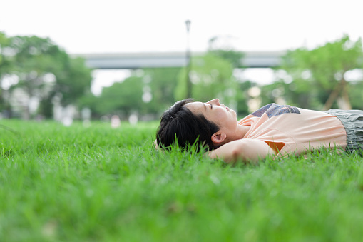 Photo of a Japanese woman lying on the green grass. She wearing pink t-shirts and close eyes.