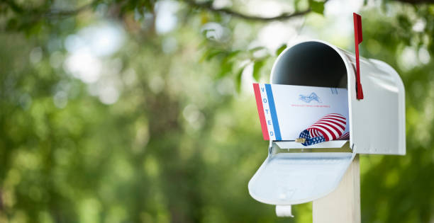 Voting By Mail Concept Voting by mail concept. Absentee ballot envelope in a mailbox against a defocused nature background. absentee ballot photos stock pictures, royalty-free photos & images